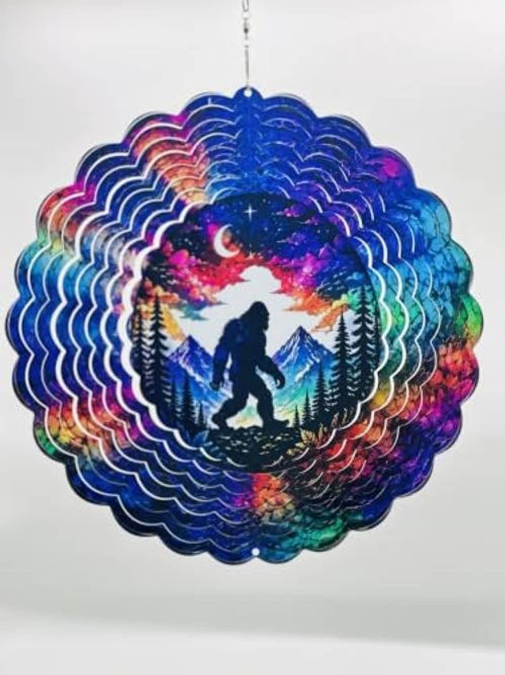 Close-up of hanging Bigfoot wind spinner with moonlit mountains and pine trees