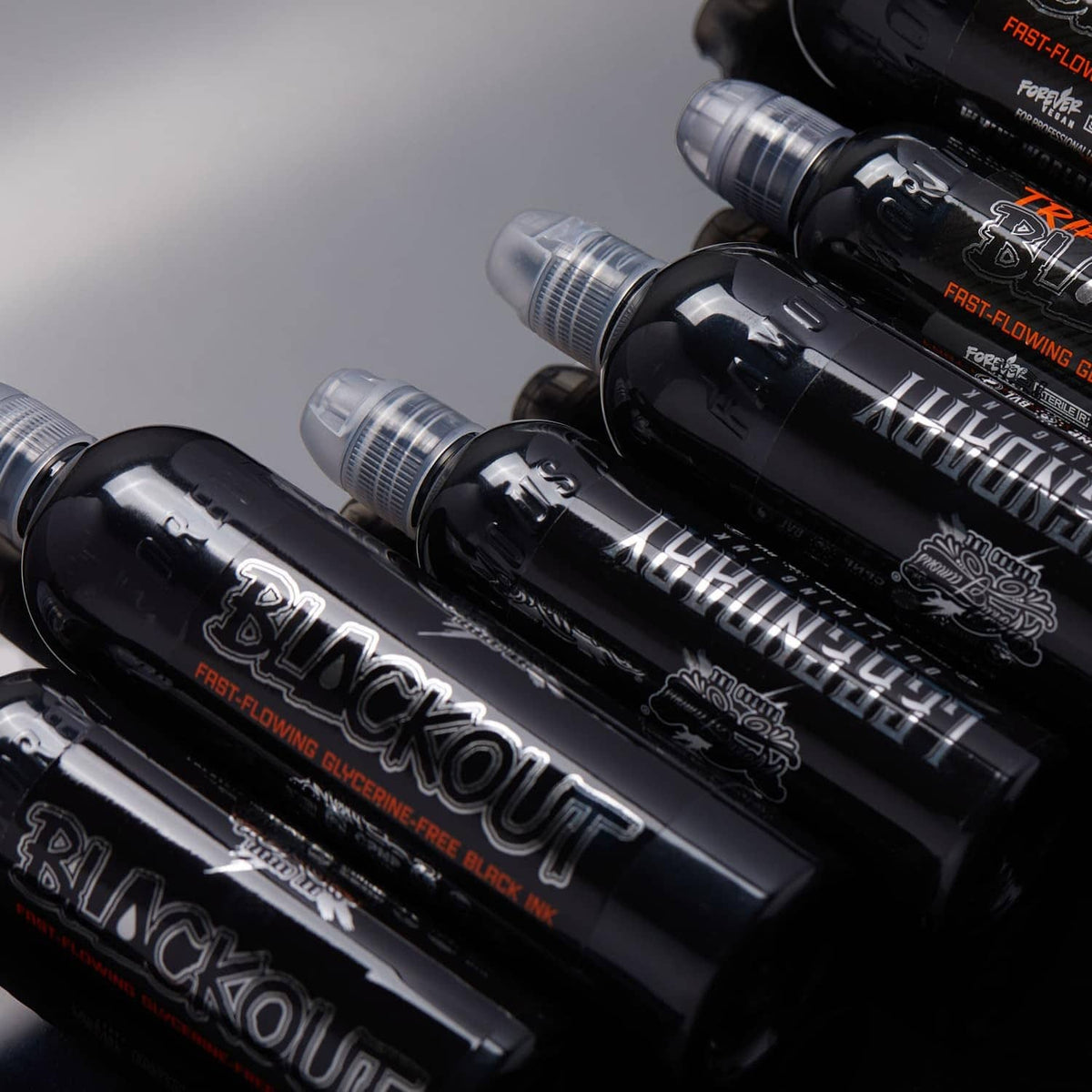 Multiple black tattoo ink bottles with clear caps in a diagonal row