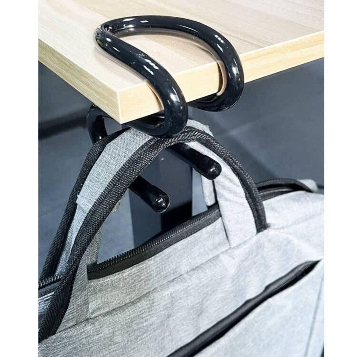Black clamp-on bag hook fastened to a gray backpack strap near a zipper