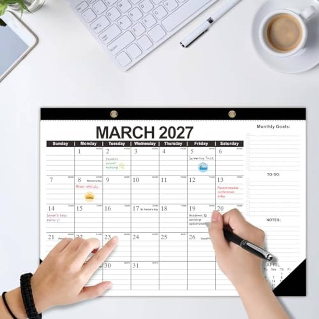 March 2027 desk calendar with monthly grid; hands pointing and writing with pen