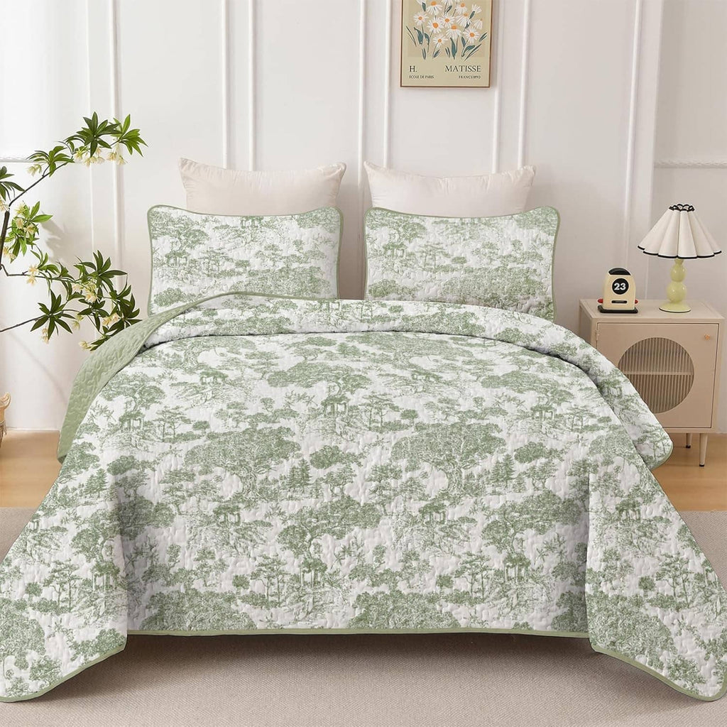Sage green botanical quilt with two square pillow shams, laid flat on a bed