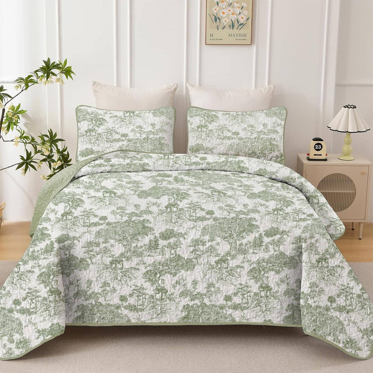 Sage green botanical quilt with two square pillow shams, laid flat on a bed