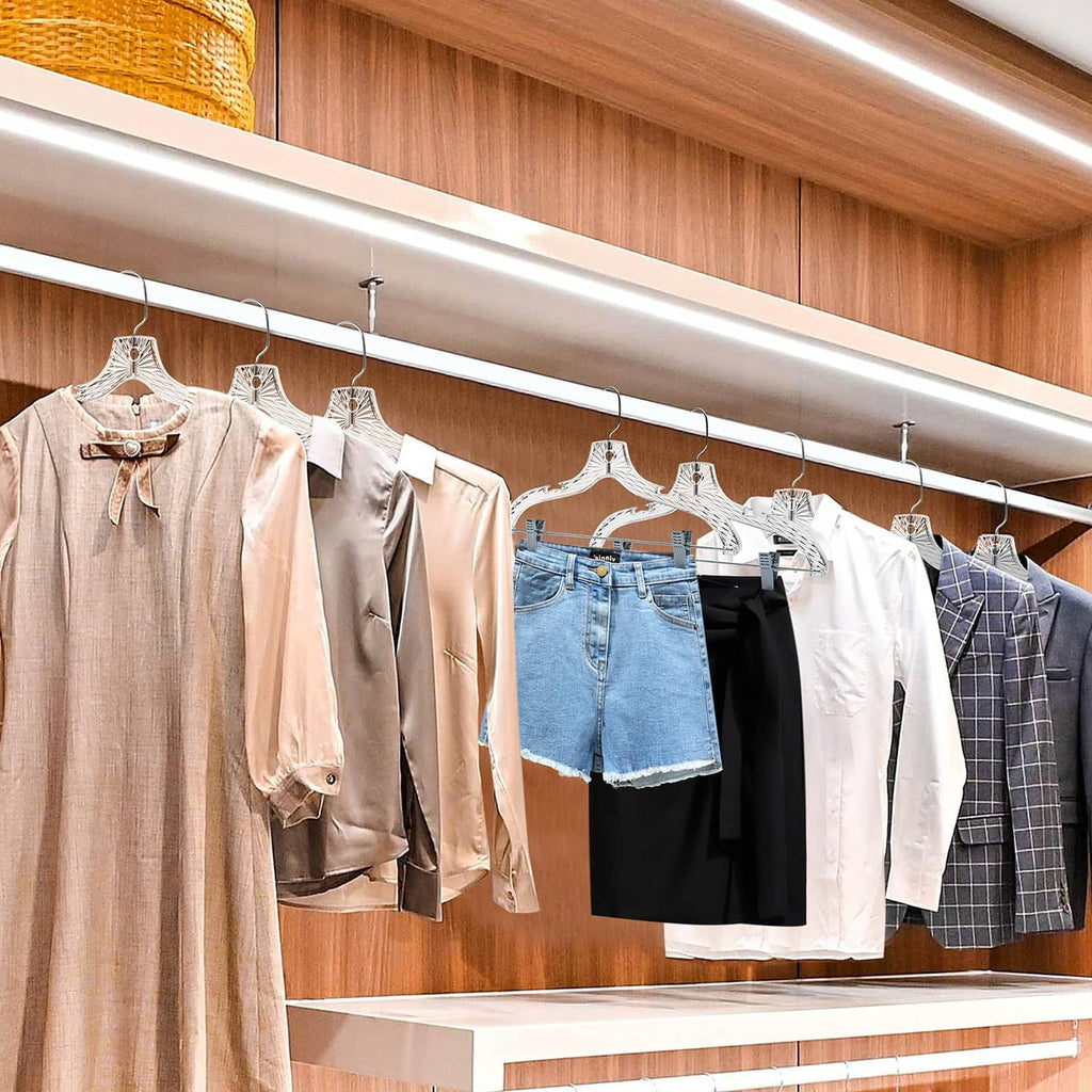 Clear plastic hangers with metal clips holding shirts and pants on closet rod