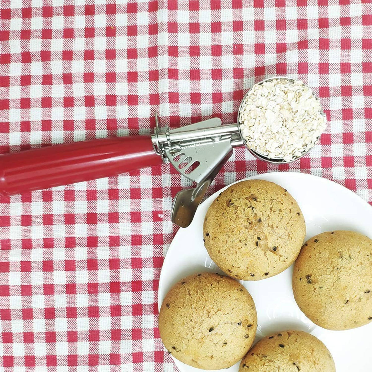 Red cookie scoop releasing cookies onto a plate