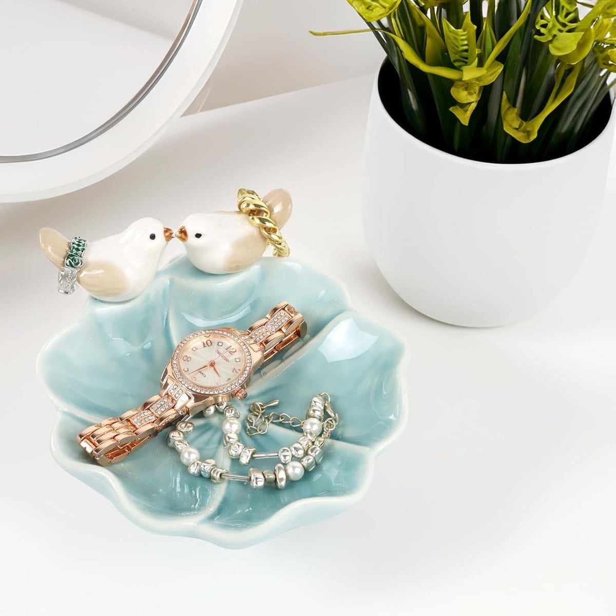 Ceramic lotus leaf jewelry tray with two white bird ring holders holding bracelets and a watch