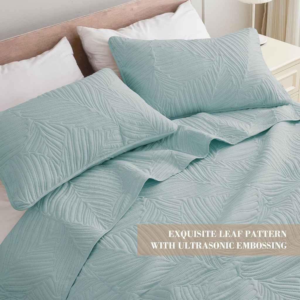 Aqua blue quilt with raised leaf pattern and embossed texture, layered on bed