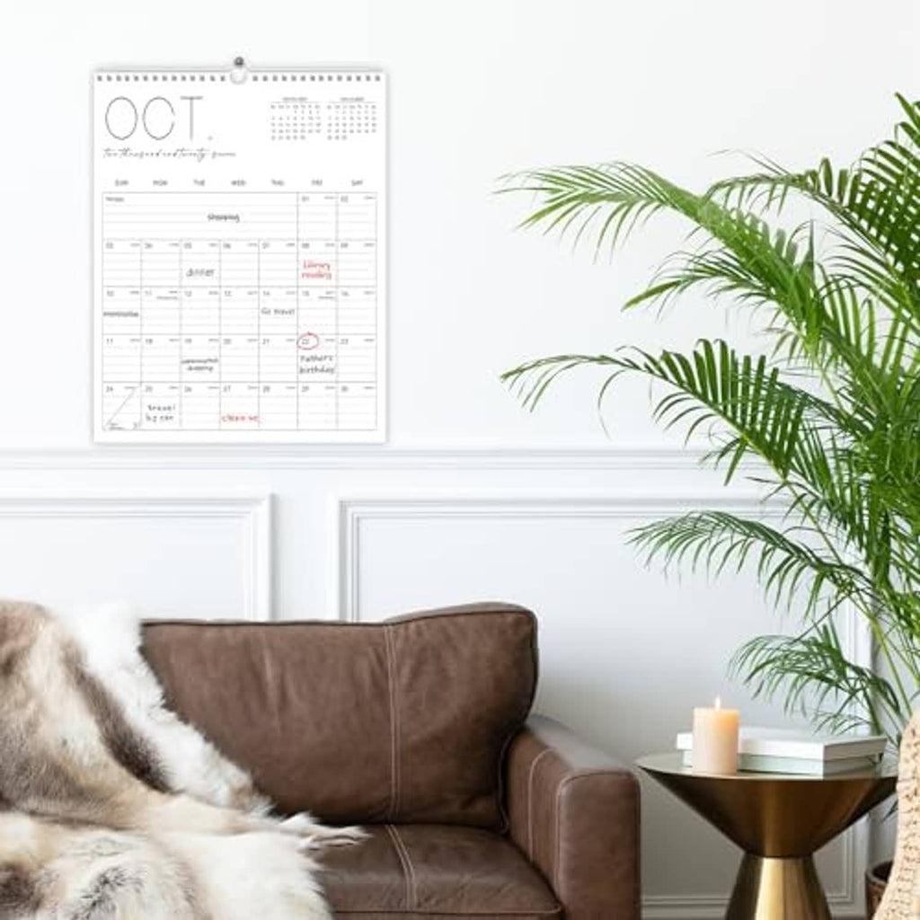 White wall calendar hanging on wall above a couch, monthly grid visible