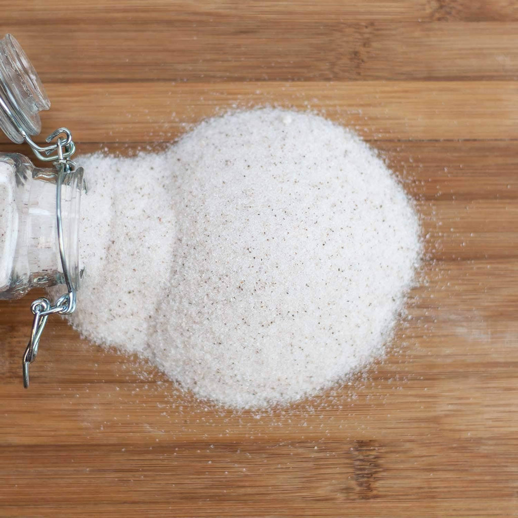 Mound of fine white sea salt granules on a wooden board