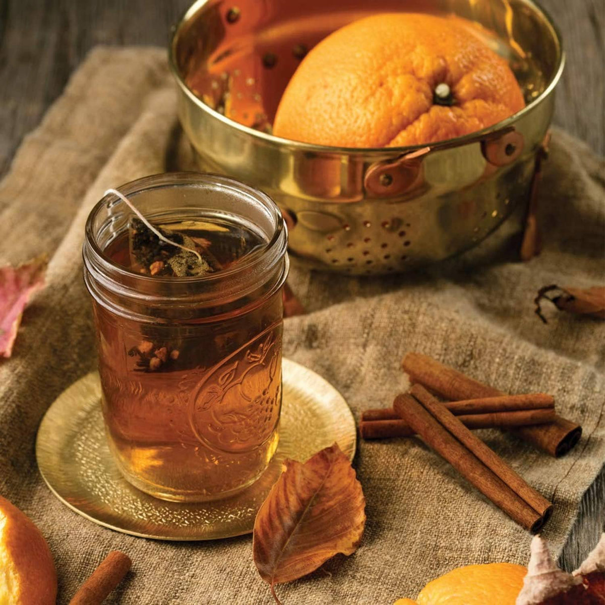 Brewed black tea in glass cup with spices, orange, and metal strainer