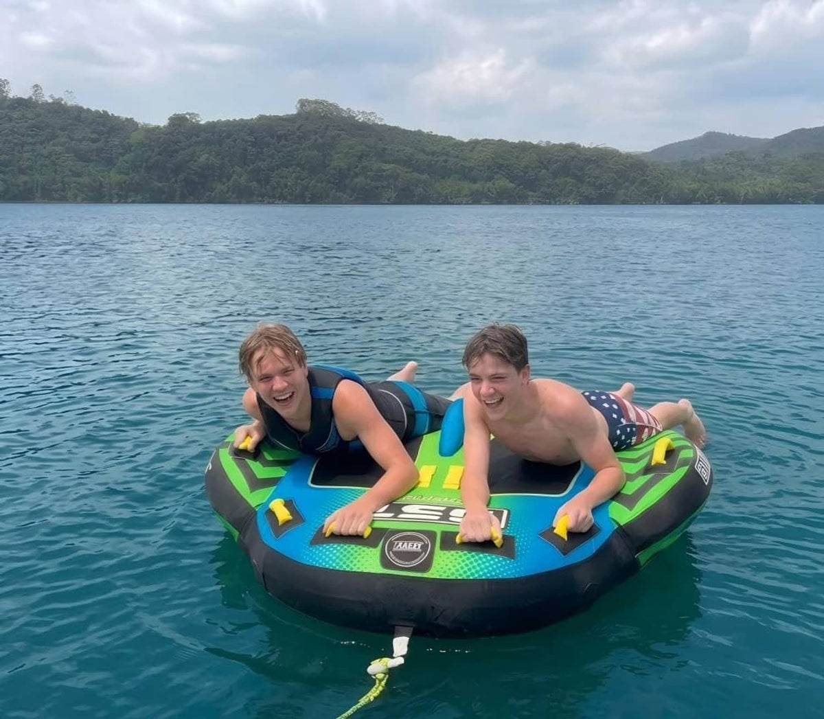 Two-person deck-style boat tube with green-and-blue seat pads and center fin