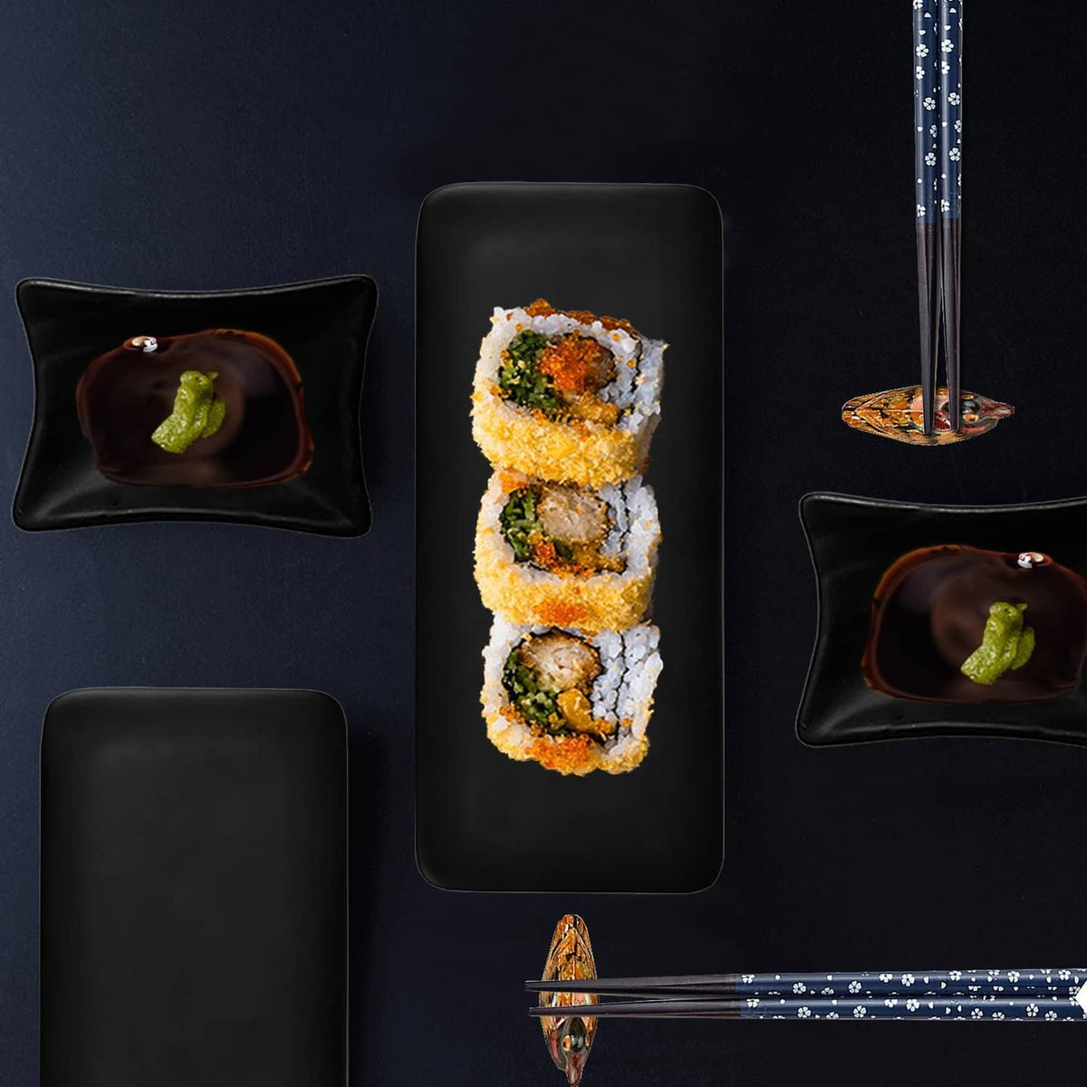 Black sushi serving set with stacked rolls, sauce dish, and chopsticks