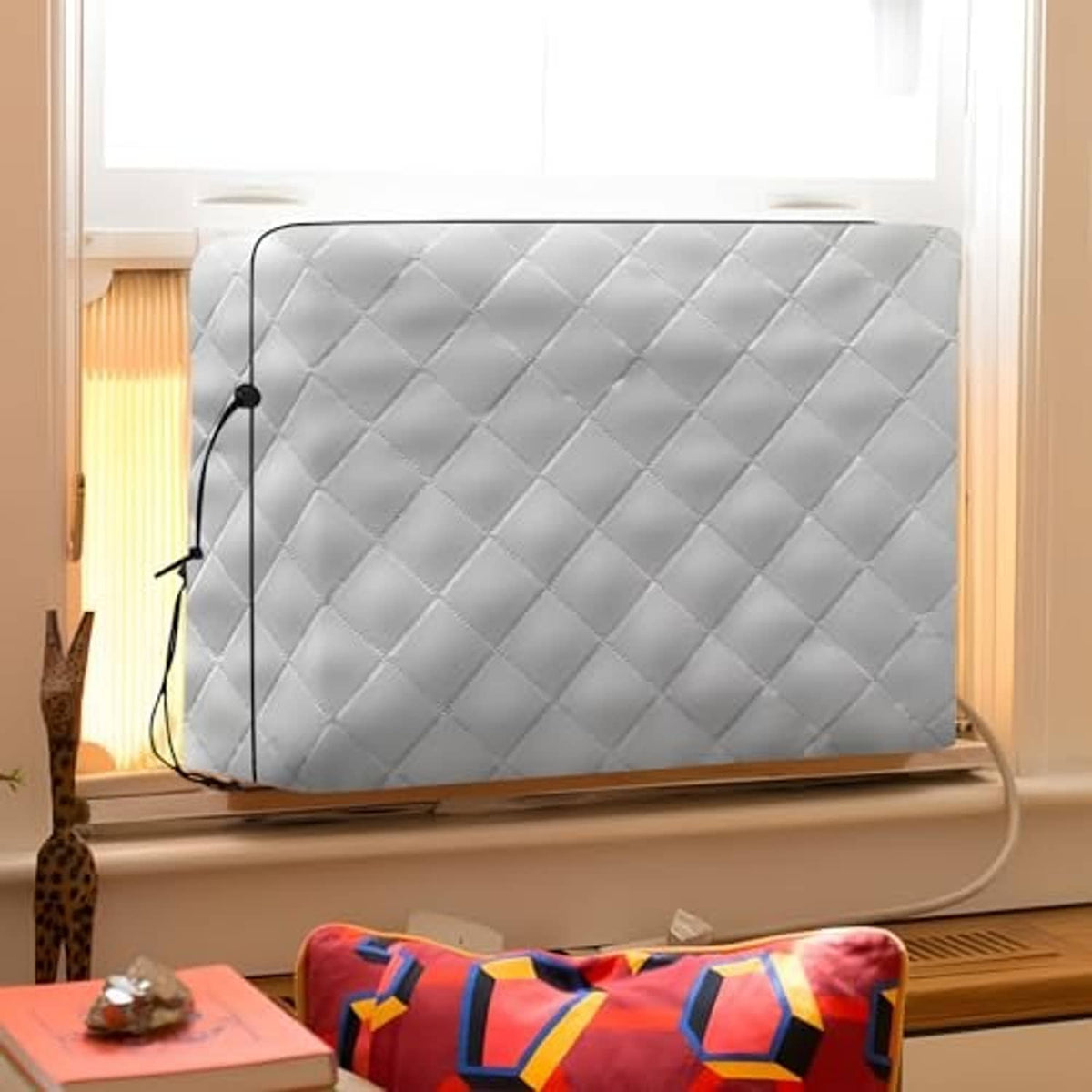 Gray quilted indoor air conditioner cover installed over a window unit with cord.