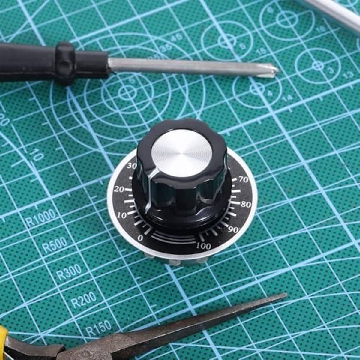 Rotary potentiometer on green cutting mat with black knob and metal scale face