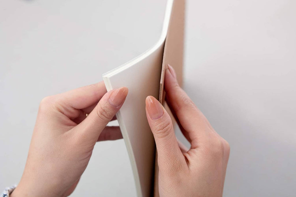 Smooth Bristol paper sheets, tape-bound pad corner held between fingers.