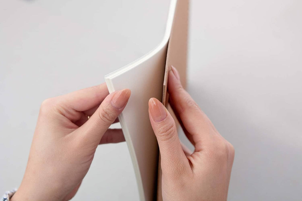 Smooth Bristol paper sheets, tape-bound pad corner held between fingers.