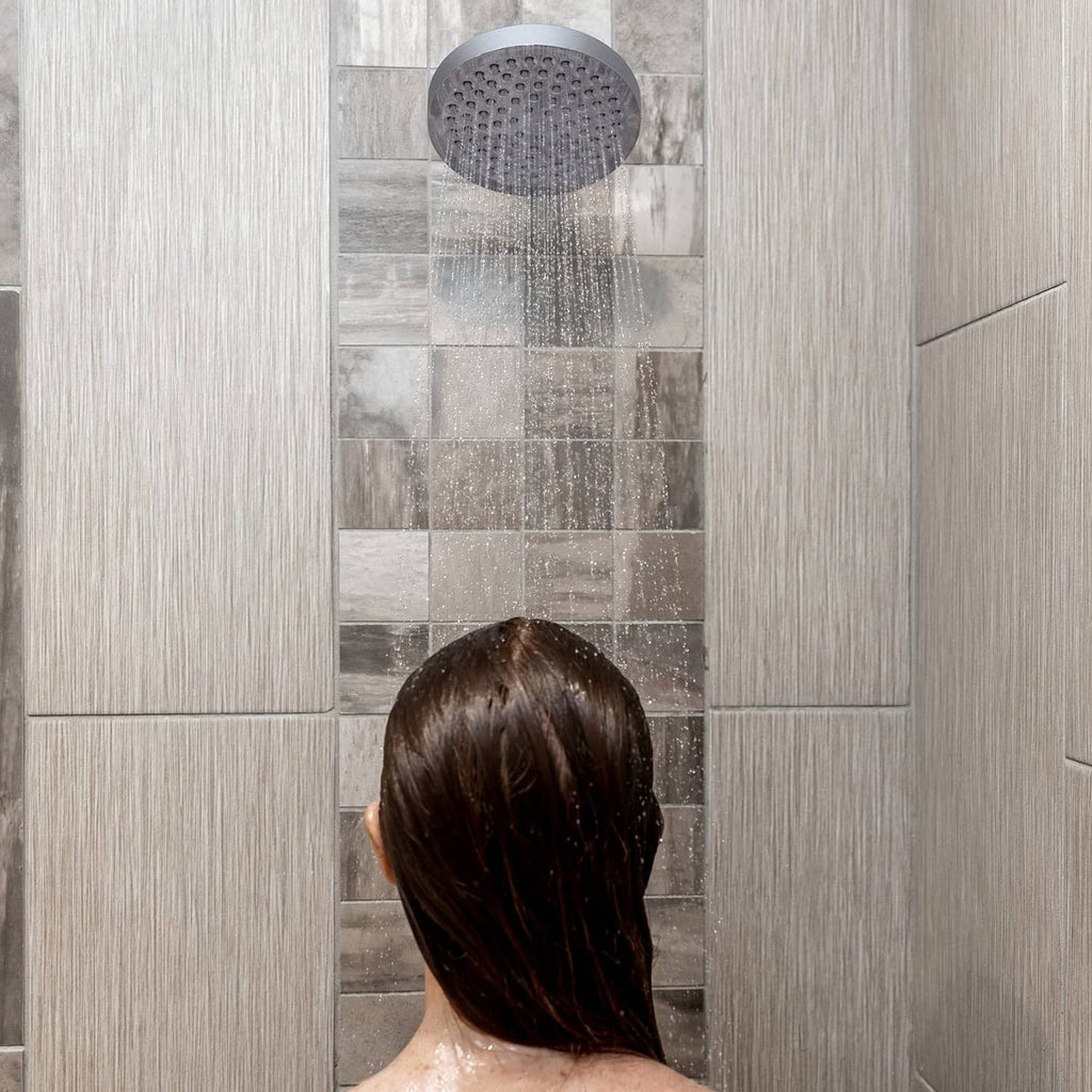 Charcoal grey 6-inch rain shower head spraying water in a tiled shower