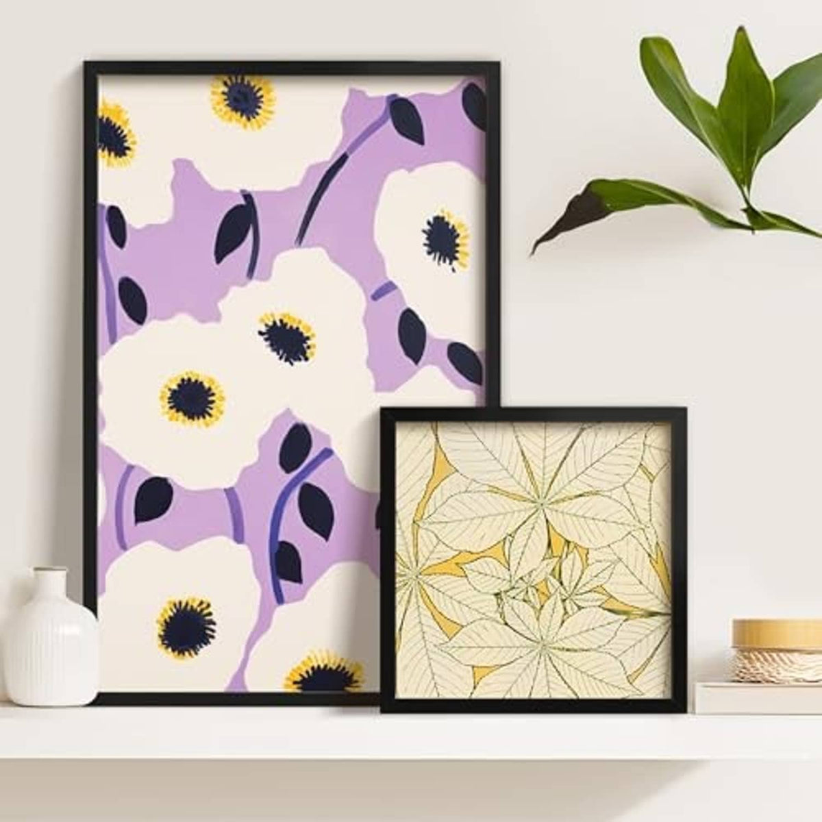 Black poster frames on a shelf with abstract and leaf artwork