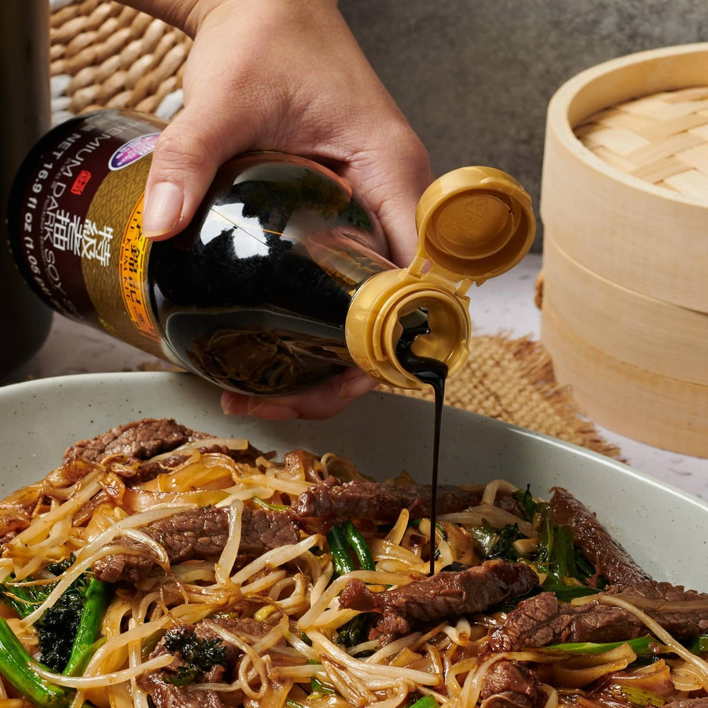 Hand pouring Lee Kum Kee dark soy sauce from bottle over noodles