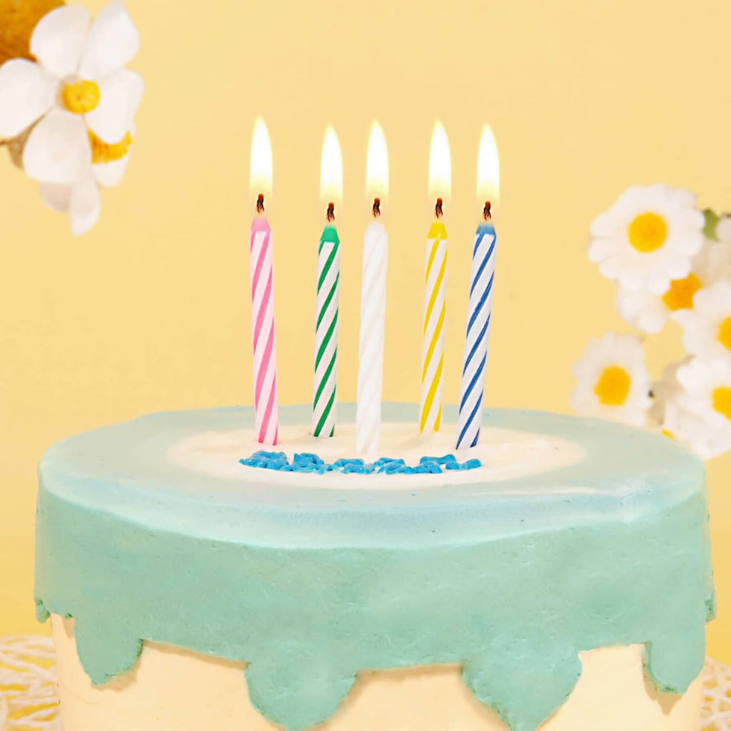Lit striped birthday candles on blue frosted cake with white icing and toppers