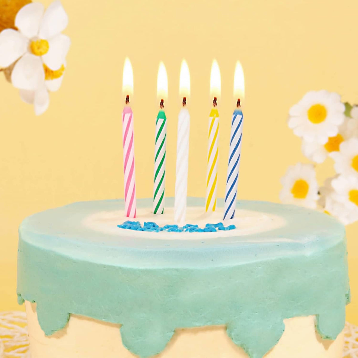 Lit striped birthday candles on blue frosted cake with white icing and toppers