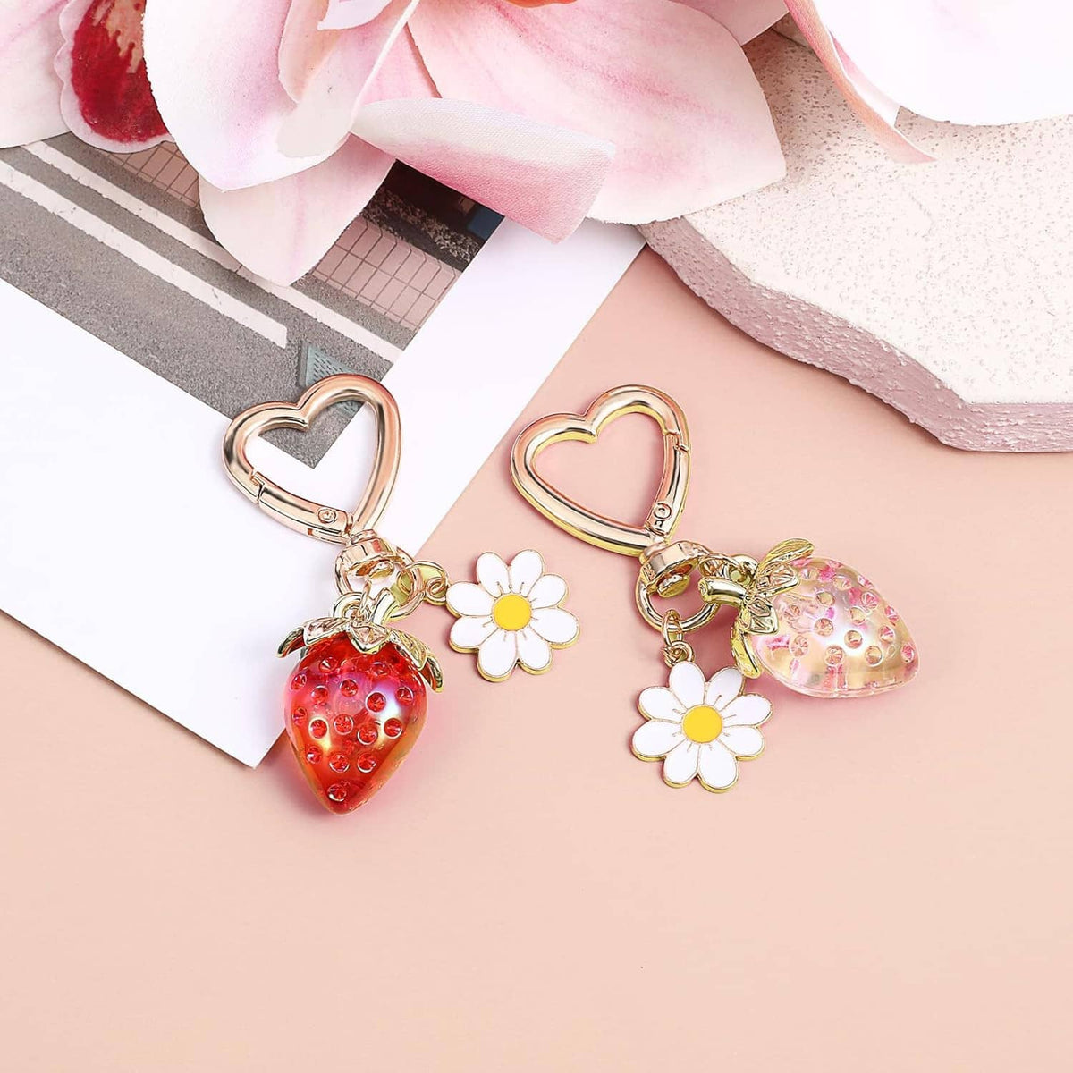 Two gold heart keychains with red and pink strawberry charms and white daisy pendants