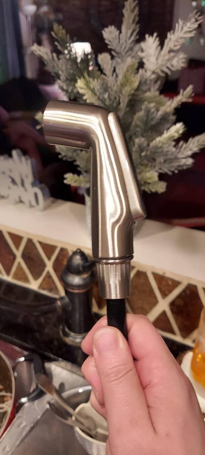 Brushed nickel kitchen sink side spray being held by hand