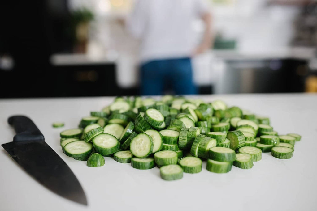 Sliced cucumbers on a white countertop with a chef knife nearby