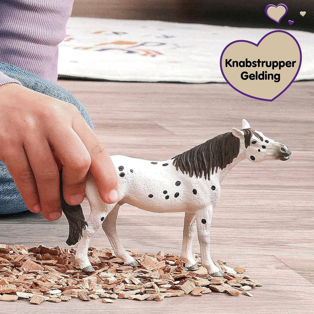 Leopard-spotted horse toy figure with black mane and tail, near a human hand.
