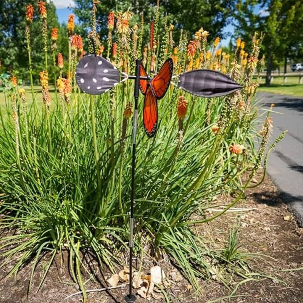 Monarch butterfly wind spinner on a stake with orange wings amid tall greenery