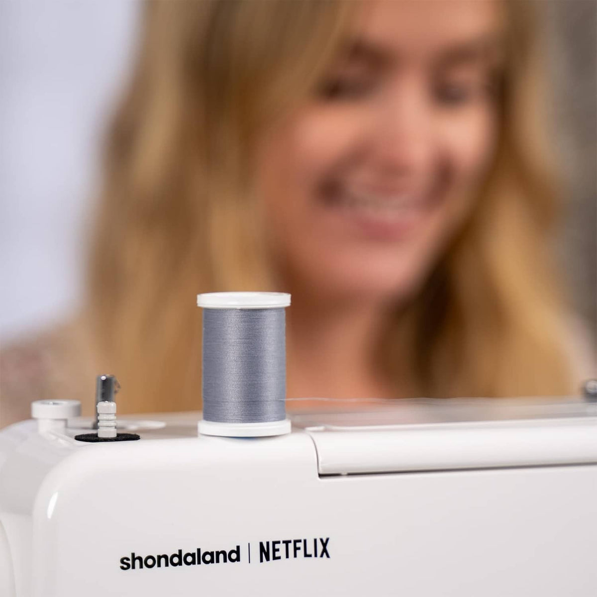 White sewing machine with 'shondaland | NETFLIX' text and tabletop bobbin spool