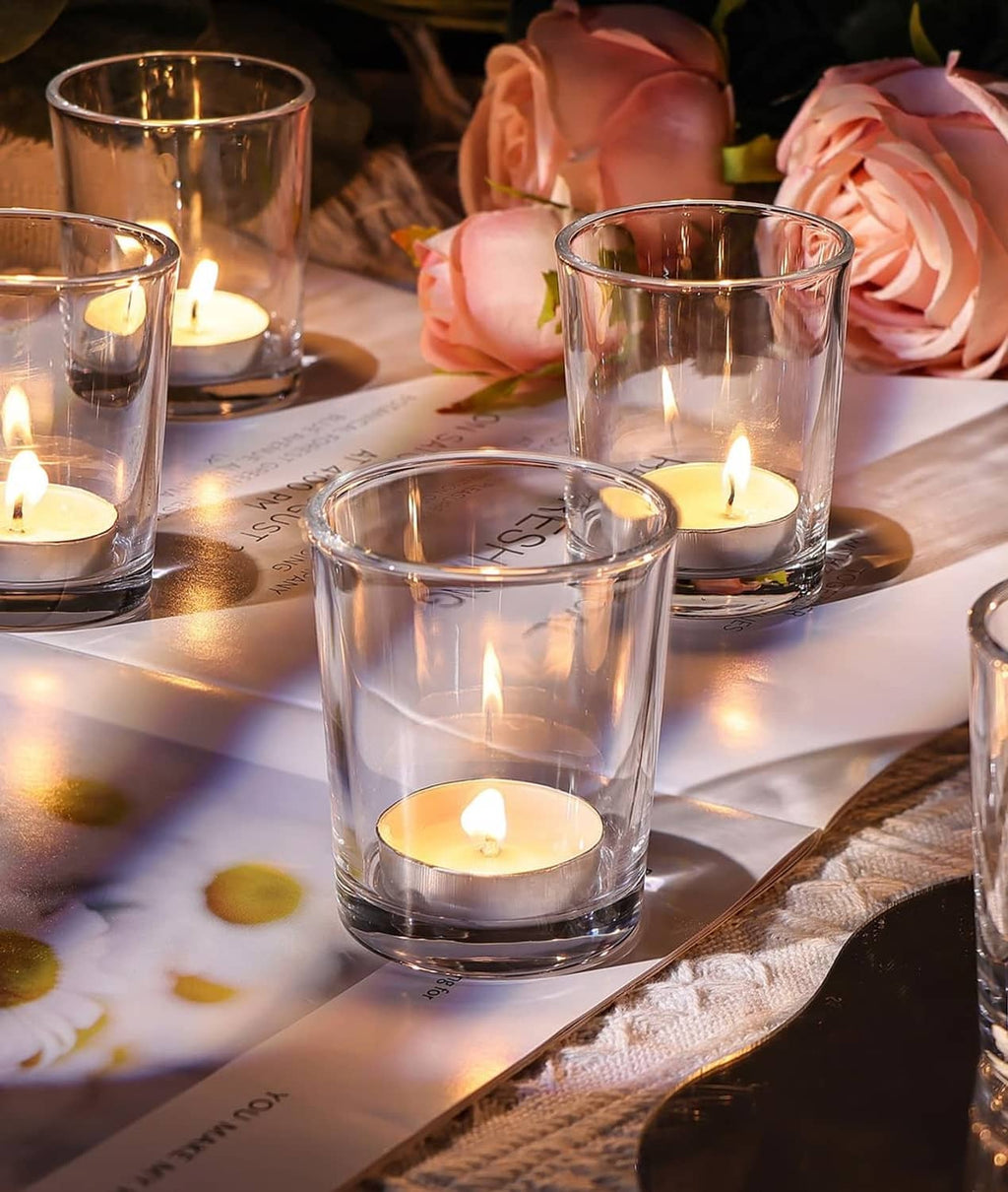 Clear glass votive candle holders with lit tea lights, cylindrical cups