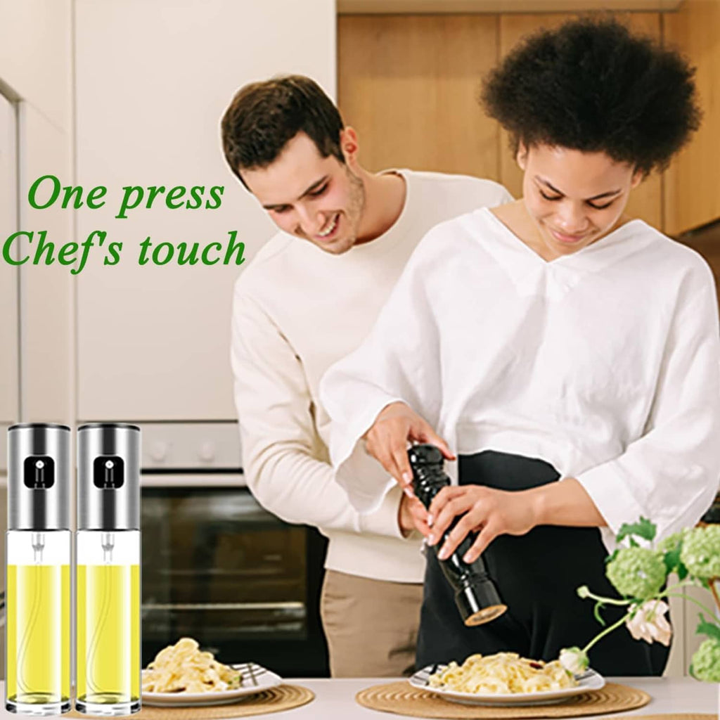 Stainless steel oil sprayer with clear bottle and yellow liquid on countertop near chefs