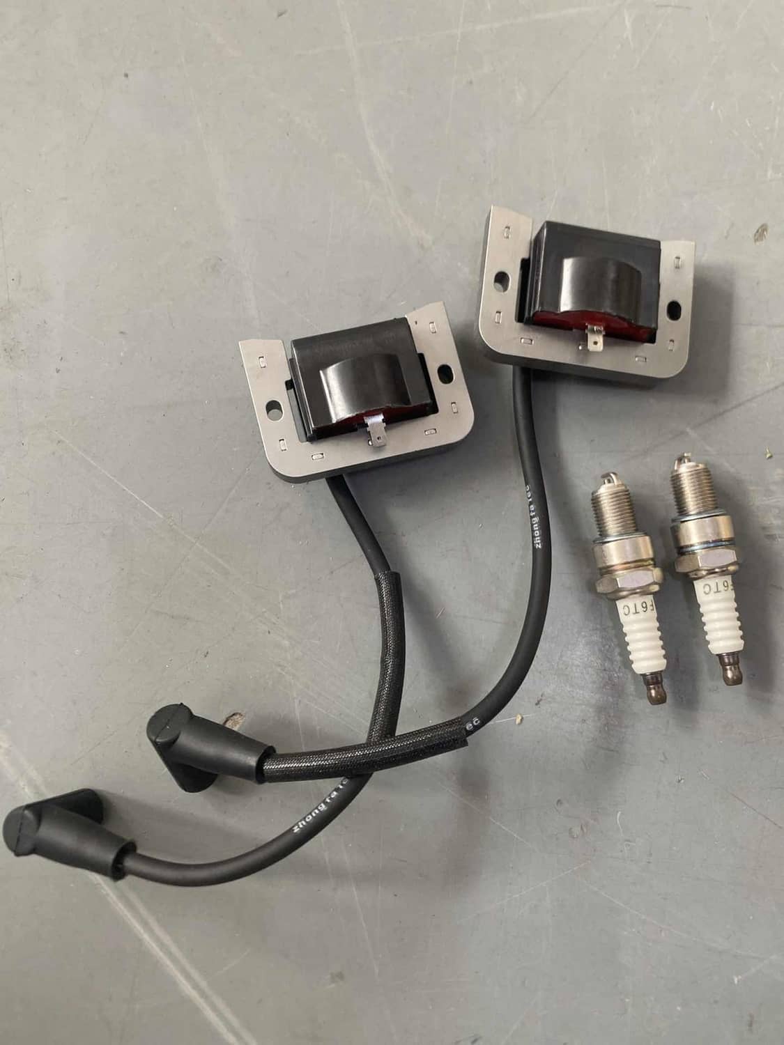 Two ignition coil modules with black wiring and two spark plugs, laid on surface
