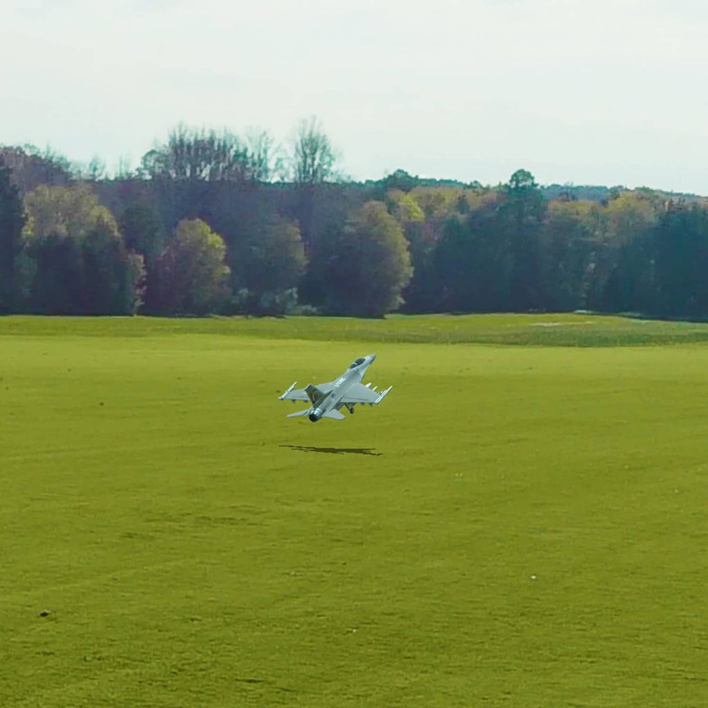 White RC airplane flying low over a green field