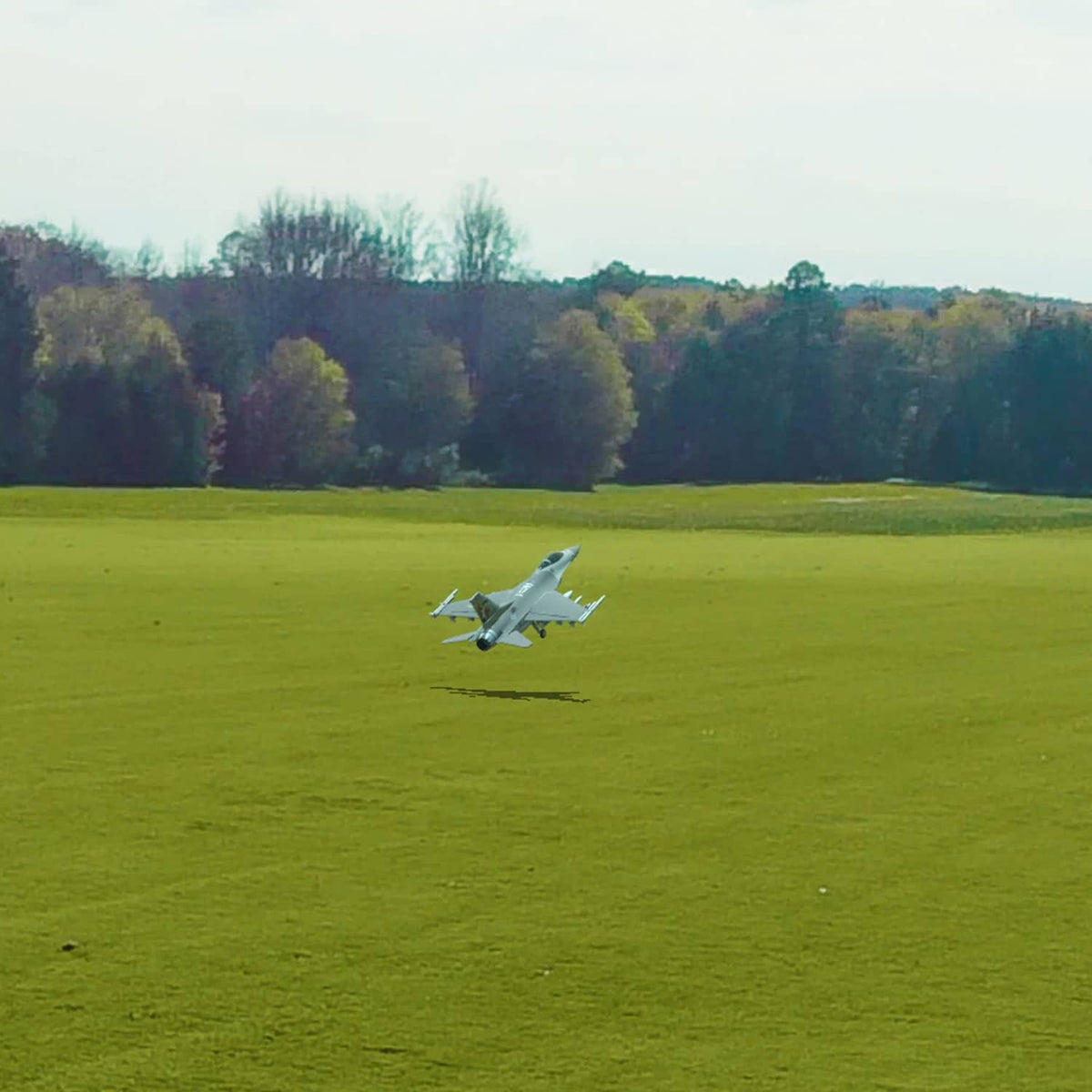 White RC airplane flying low over a green field