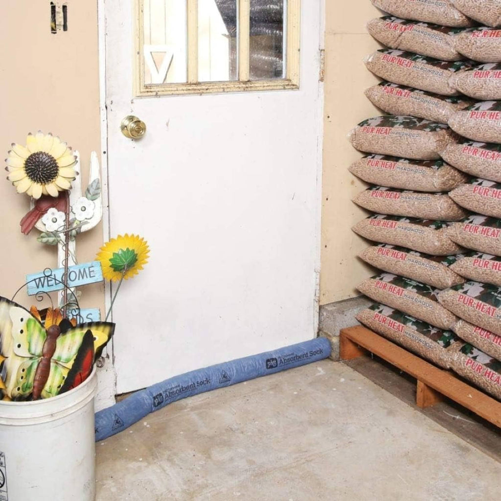 Blue absorbent sock barrier laid in an L-shape on the floor near stacked bags