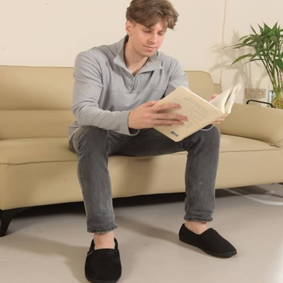 Black moccasin house slippers with thick sole and fuzzy lining on a seated man.
