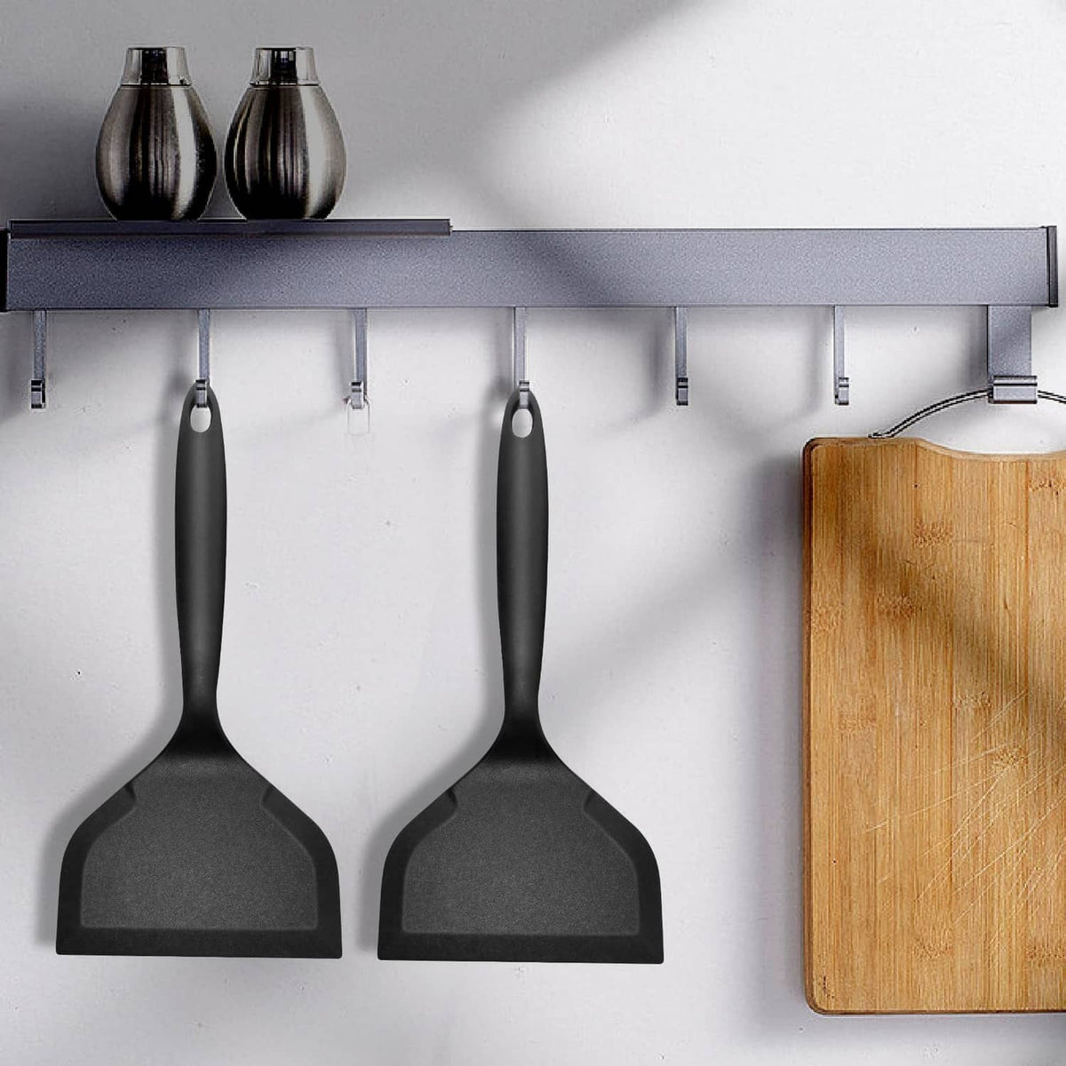 Set of black silicone pancake flippers hanging on a rack, wide flat heads