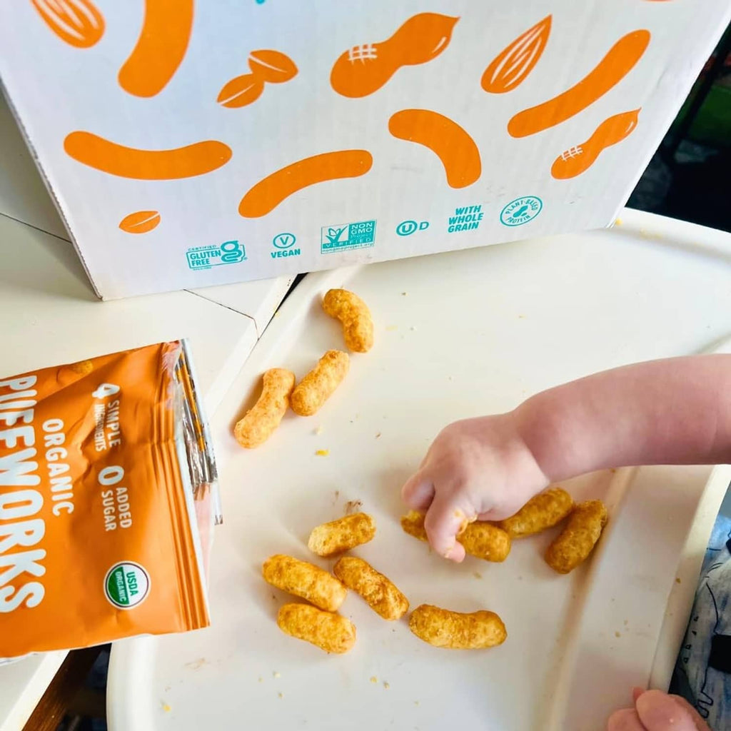 Hand reaching for organic peanut butter puff snacks from an open box