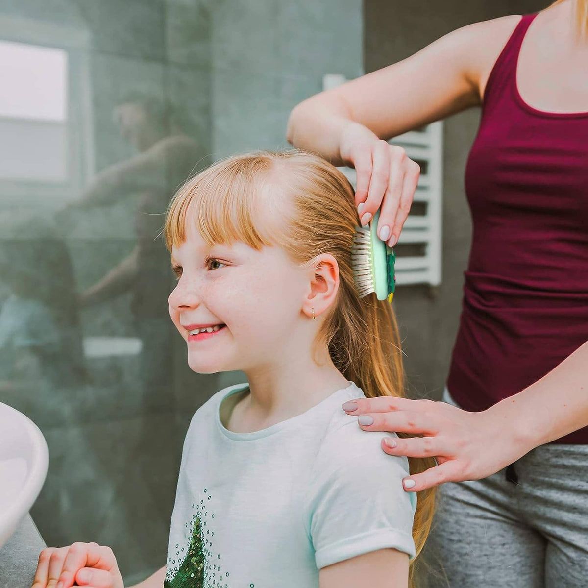 Mint kids hair brush in use on a child’s hair, with green dinosaur handle