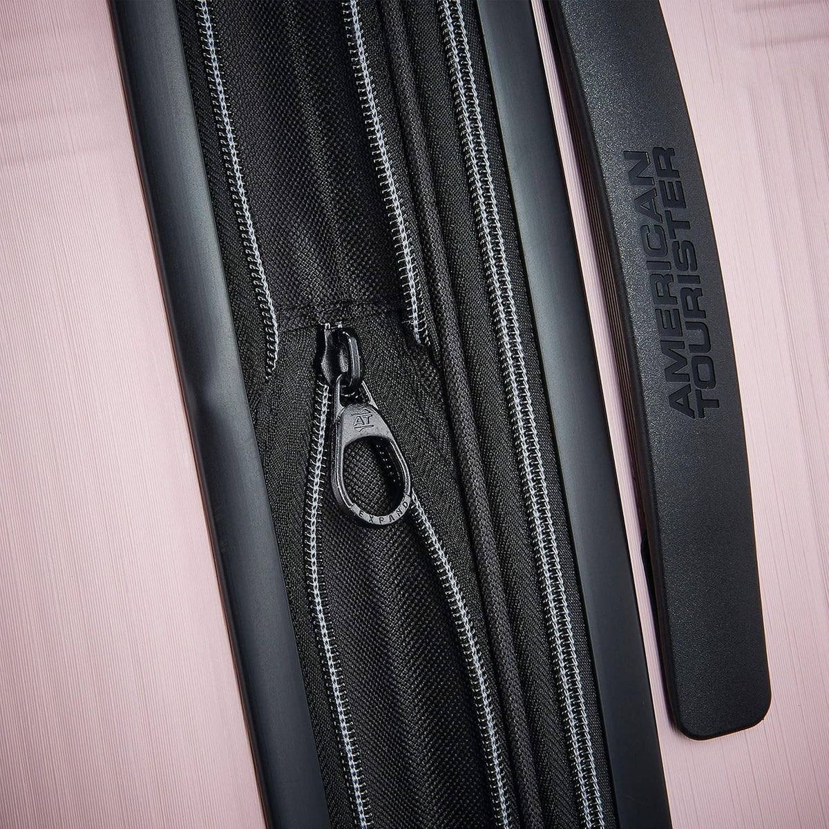 Pink hard-shell luggage close-up of black zipper track and zip pull with American Tourister