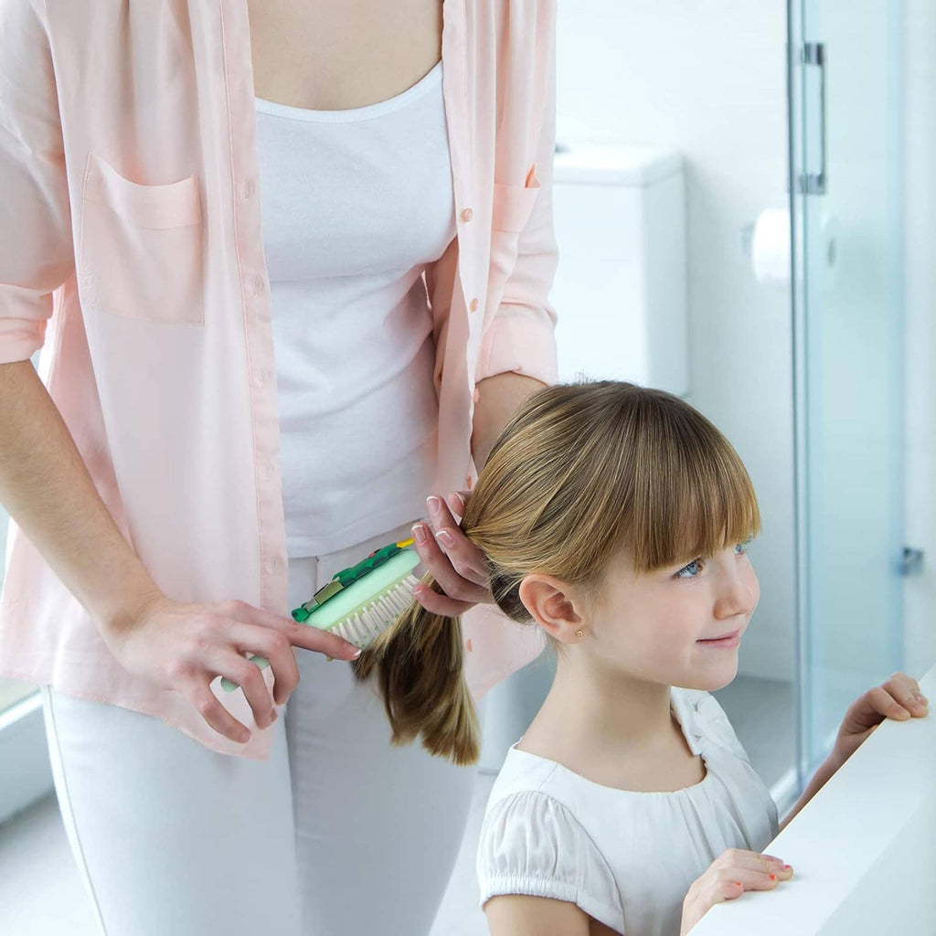 Kid holding a mint hair brush while smoothing hair, dinosaur-themed design on handle