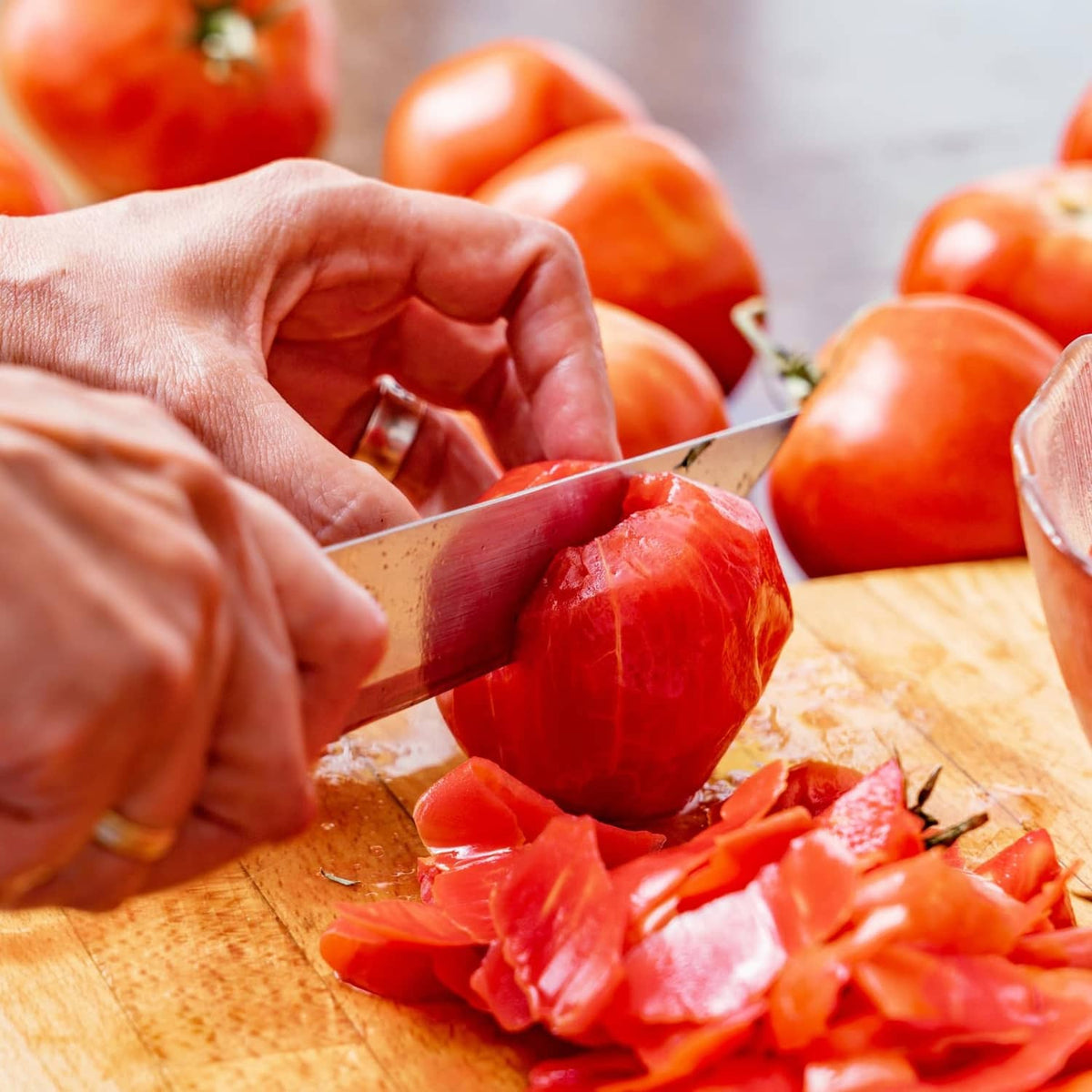 Hand slicing peeled tomatoes on a wooden board