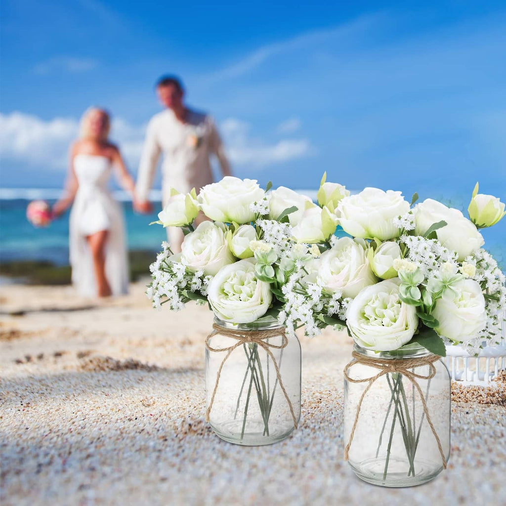 Two mason jar centerpiece vases with faux white roses and green foliage bouquets