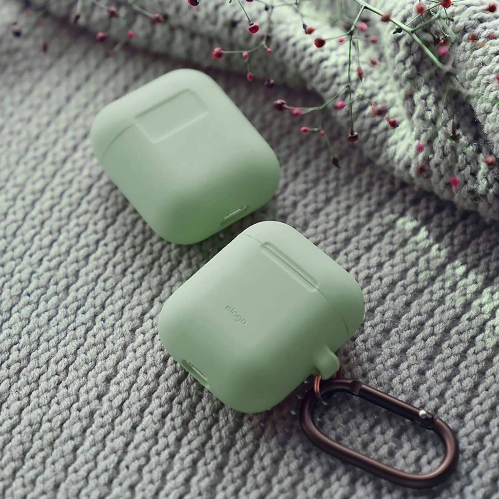 Mint green silicone AirPods case with bronze carabiner clip, close-up on fabric
