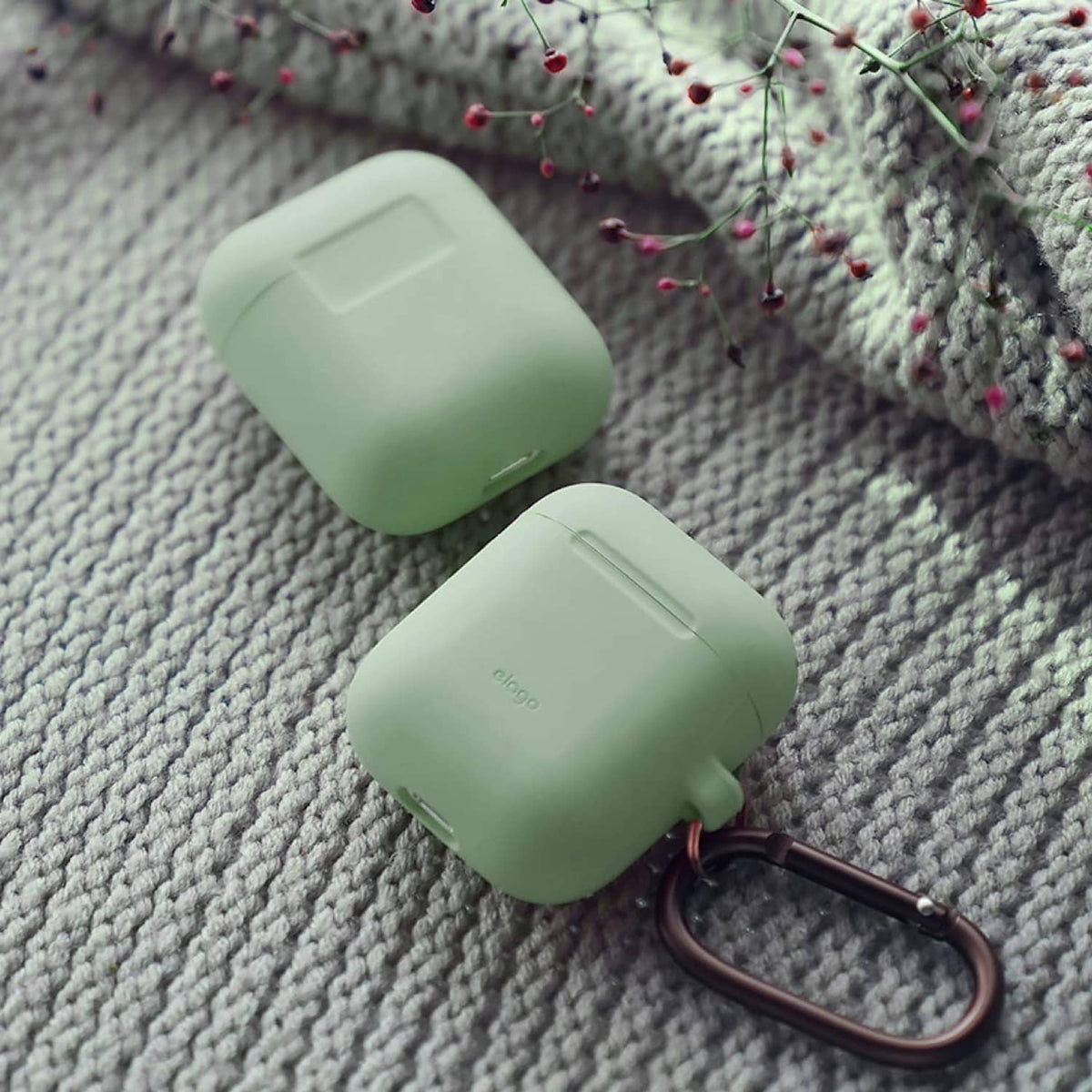 Mint green silicone AirPods case with bronze carabiner clip, close-up on fabric