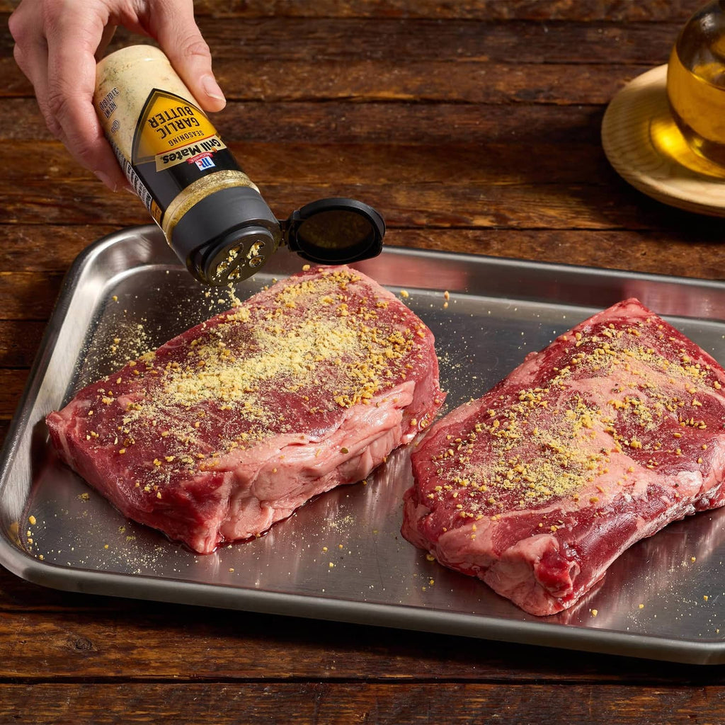 Garlic butter seasoning bottle near raw steaks on a tray