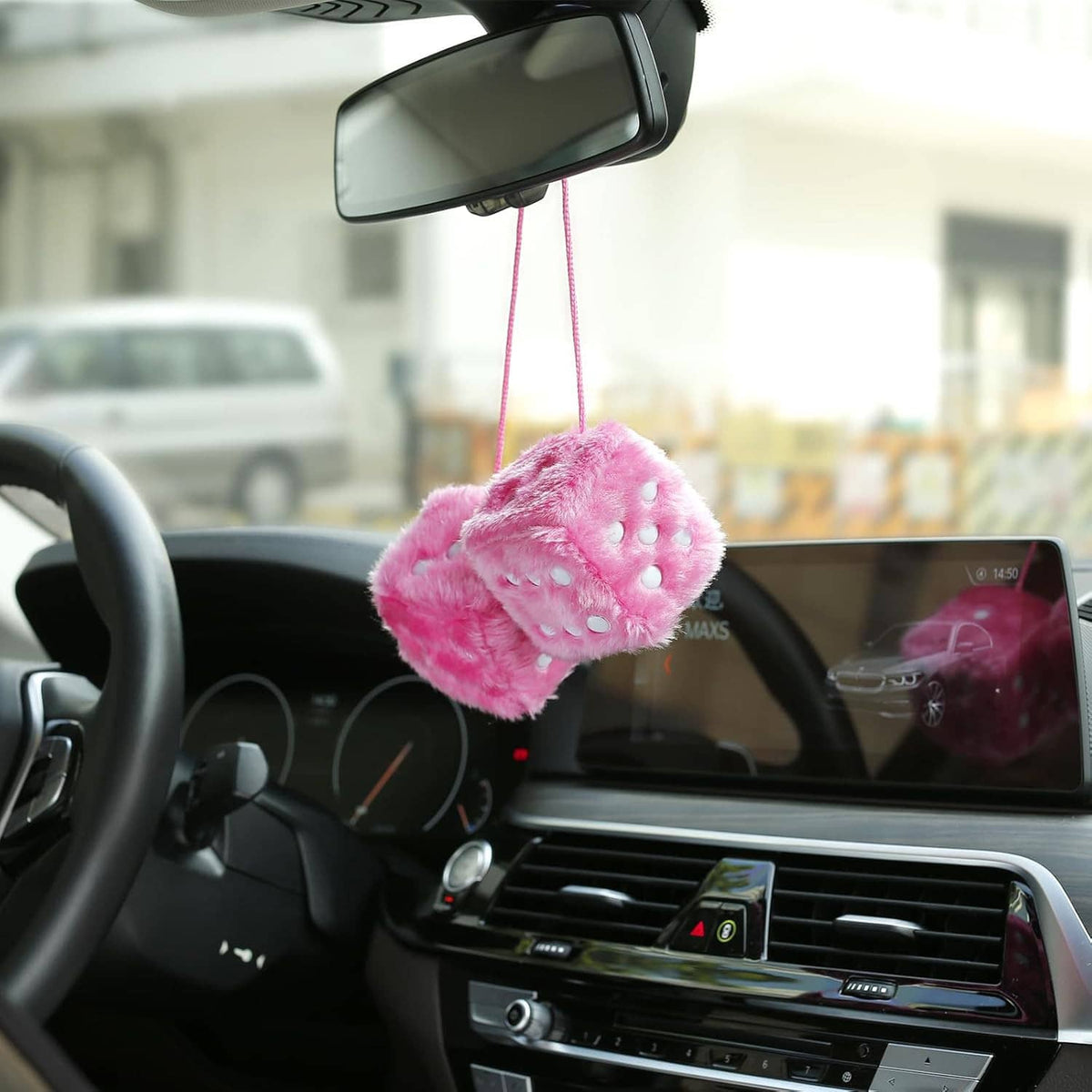Pink plush rearview mirror dice hanging from twin strings inside a car