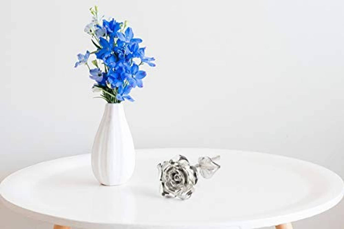 Silver tin rose ornament on a tabletop with a white vase of blue flowers