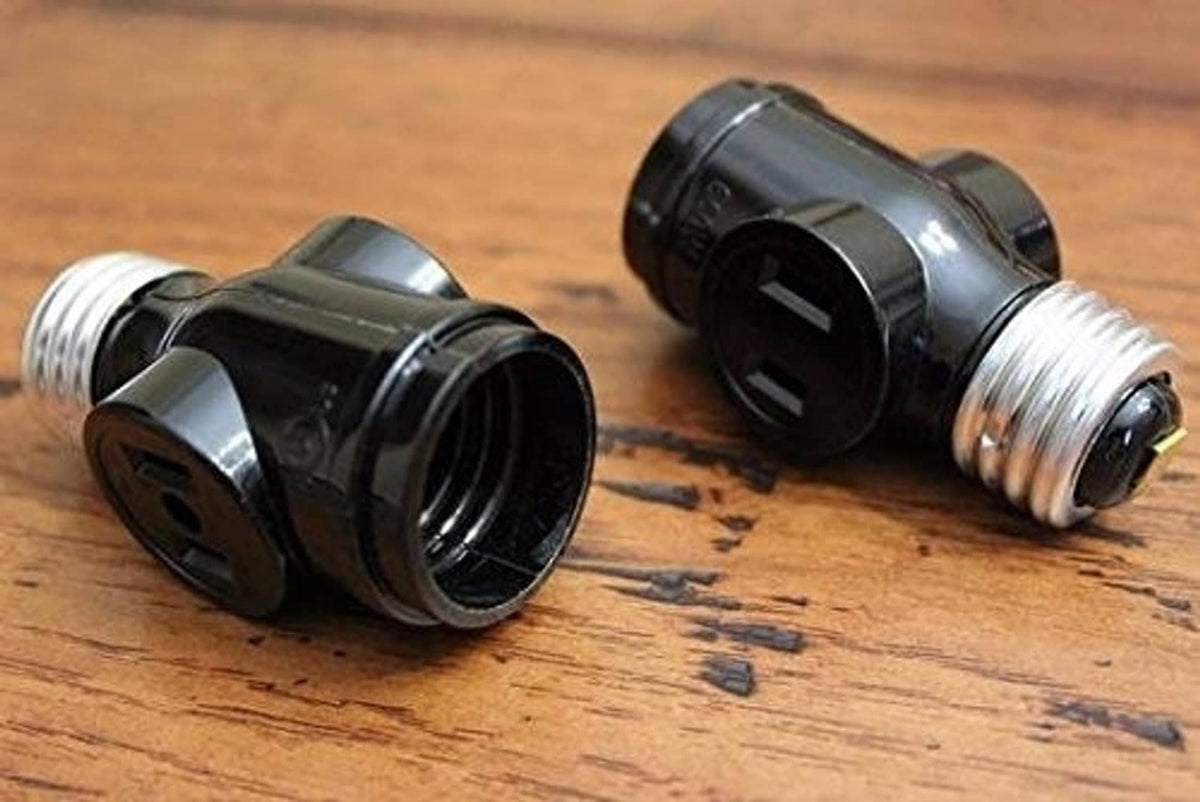 Pair of black light socket adapters with chrome screw threads on wooden surface.
